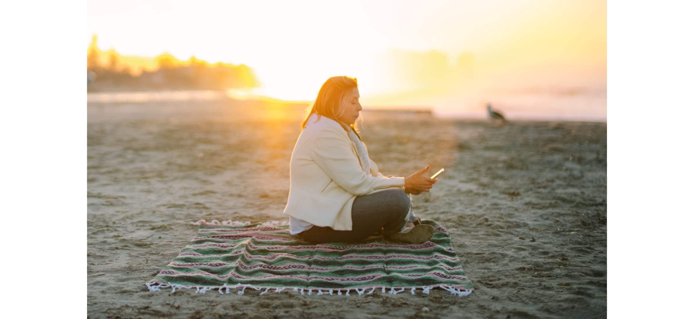 Nury sits on a San Diego beach at sunset with her phone in hand.